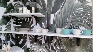 Une cuisine avec des étagères blanches où sont rangées des assiettes, des tasses et un petit appareil électroménager blanc.