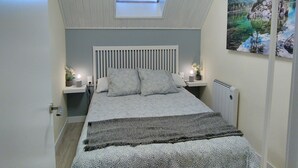 Une chambre avec une lucarne, un lit recouvert d’une literie à motifs, des lampes de chevet et un tableau accroché au mur.