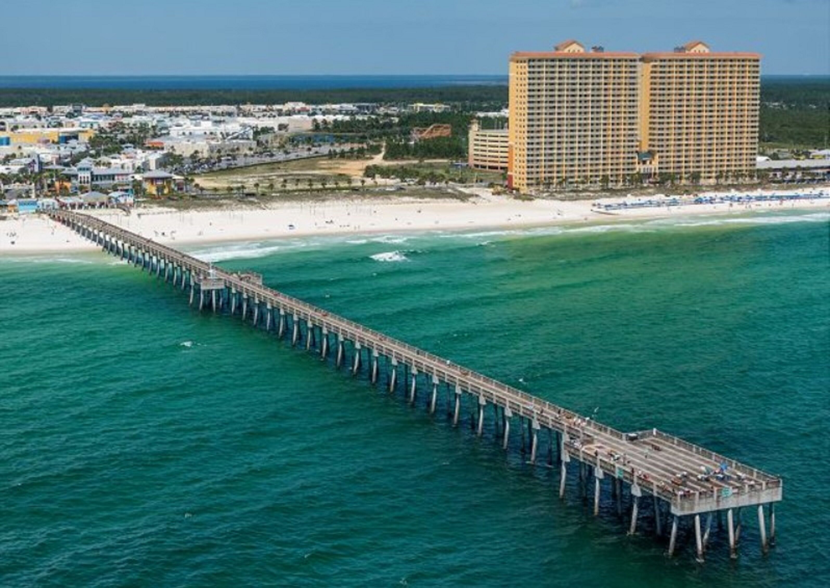 A pier extending into the ocean with a beachfront hotel in the background.