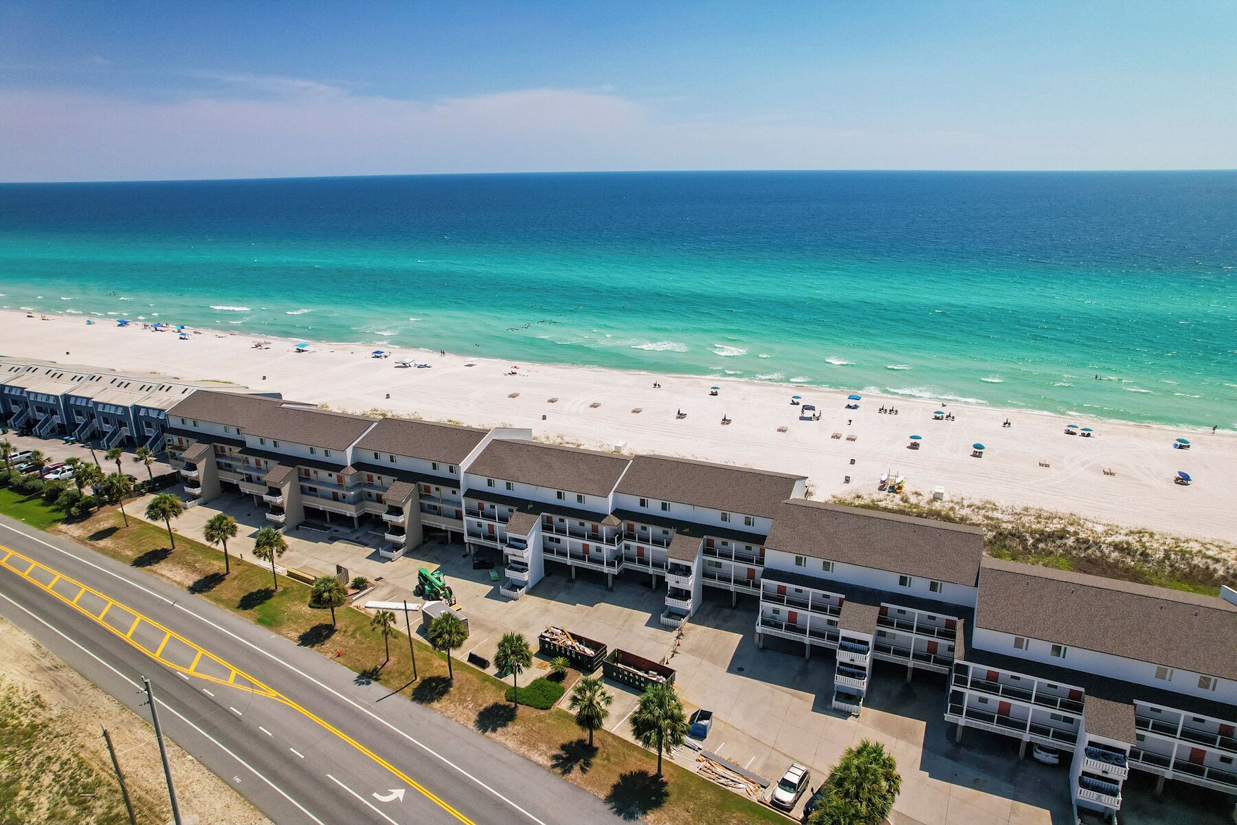 Un hotel sulla spiaggia con edifici a più piani, una spiaggia sabbiosa e una vista limpida sull'oceano.