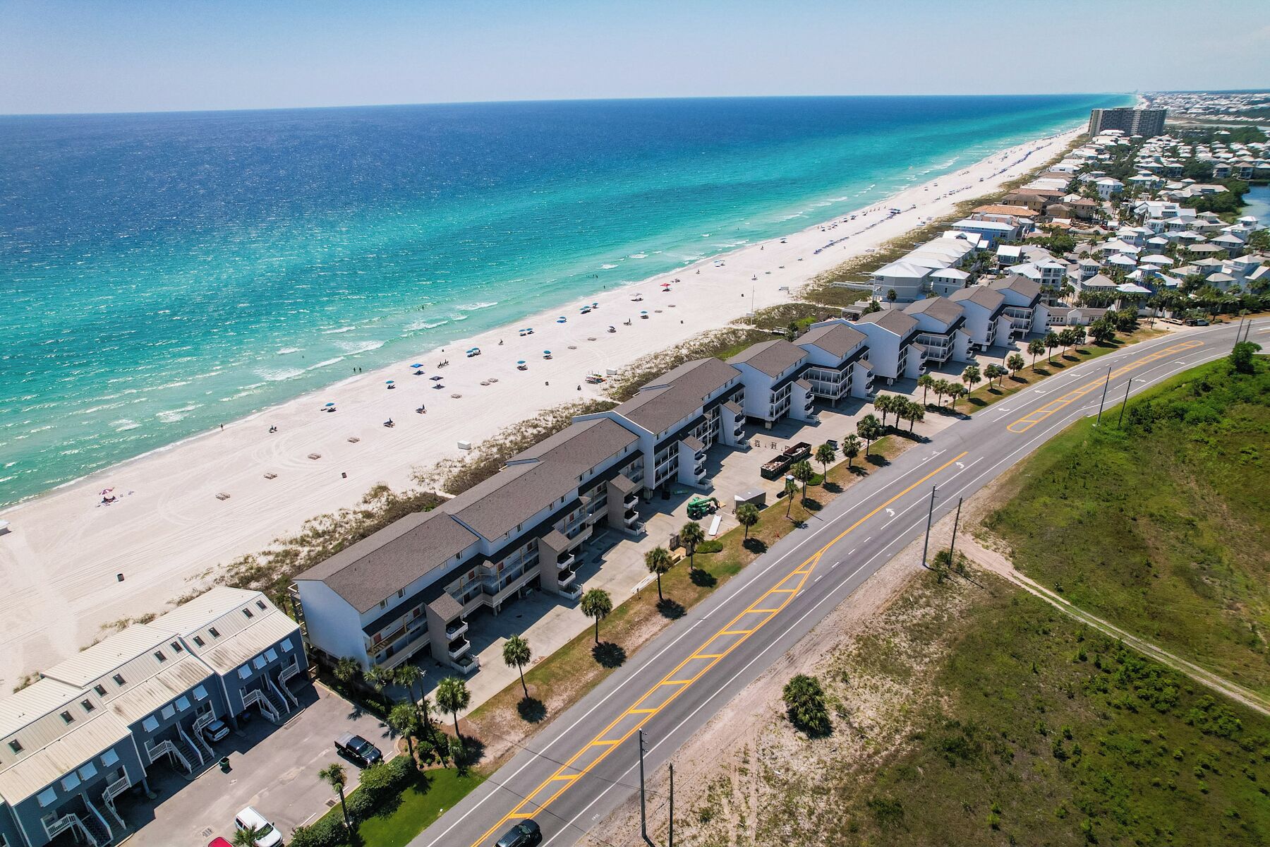 A coastal hotel with multiple-story buildings, a beach, and a road with a yellow line.