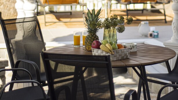 A covered outdoor seating area with a table set for two, featuring a fruit bowl, glasses, and a vase. - Ionian Star Villas by Corfu Escapes (Corfu)