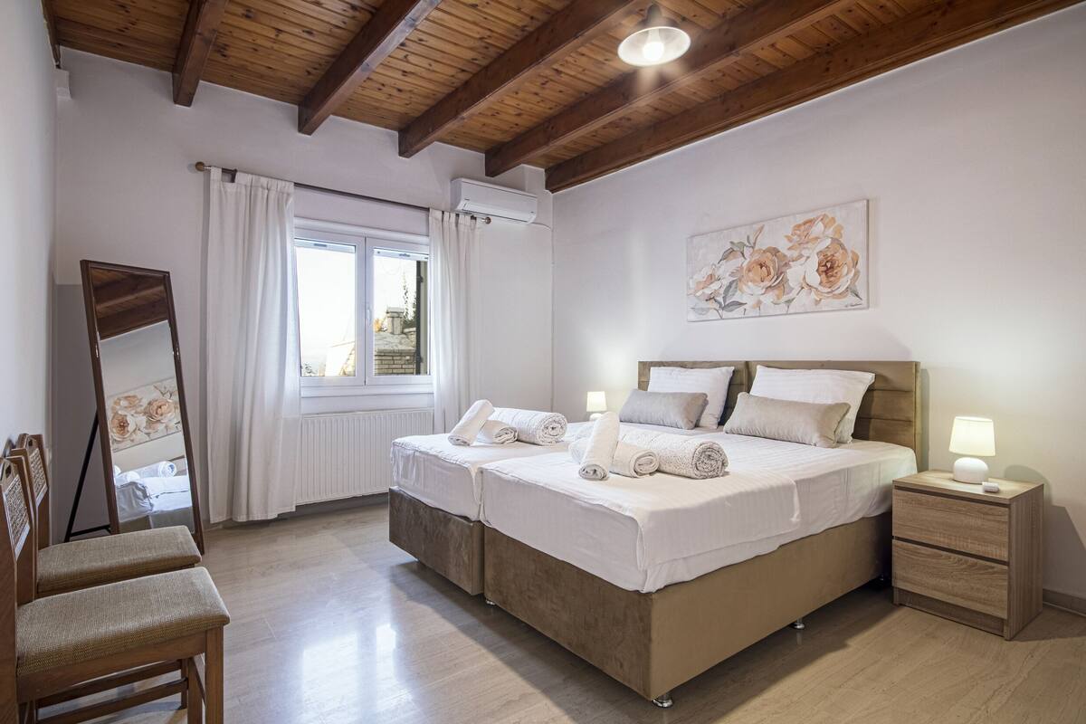 Un dormitorio con dos camas, techo de madera, un espejo grande y una ventana con cortinas.