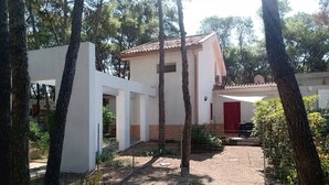 Un edificio bianco con una porta rossa, circondato da alberi e un sentiero sterrato.