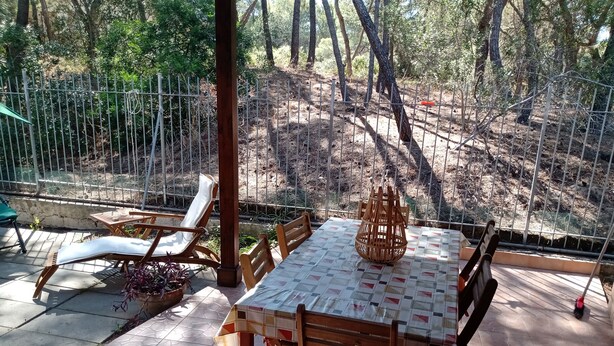 Una terrazza esterna con tavolo e sedie, circondata da una recinzione in metallo e alberi.