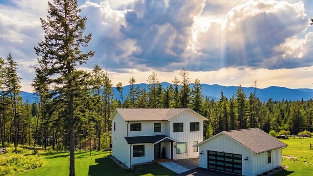 A two-story house with a garage, surrounded by a forest and mountains.