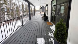 A wooden deck with a metal railing, a bench, a potted plant, and a door with glass panels.