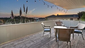 Un terrazzo in legno con mobili in vimini e luci a stringa, con vista su un paesaggio al tramonto.