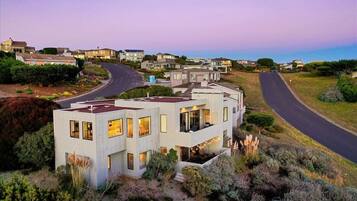 A modern two-story house with a flat roof, large windows, and a visible outdoor seating area.