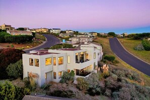 Una casa moderna de dos pisos con techo plano, ventanas amplias y un espacio exterior visible para sentarse.