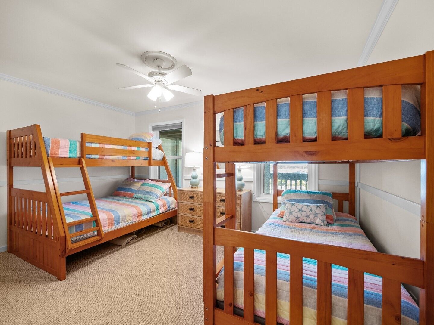 A bunk bed room with a ceiling fan, a window, and a desk with drawers.