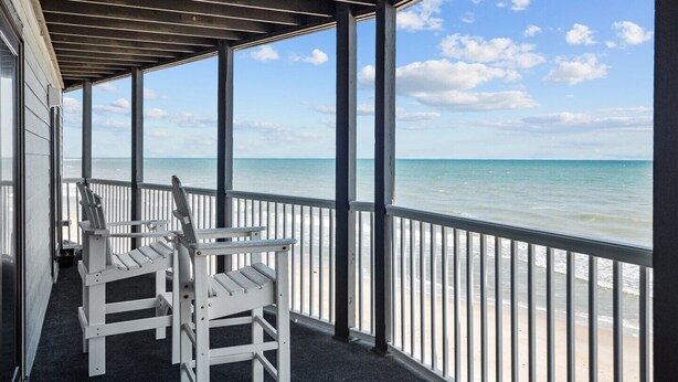 A covered outdoor area with a view of the ocean, featuring two white chairs and a railing. - 1310 Shipwatch Villas - 3BR Oceanfront Condo in North Topsail Beach with Community Pool & Elevato... (North Topsail Beach)