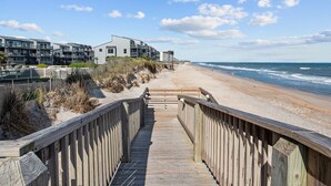 A wooden boardwalk leading to a beach with a row of modern buildings in the background. - 1310 Shipwatch Villas - 3BR Oceanfront Condo in North Topsail Beach with Community Pool & Elevato... (North Topsail Beach)