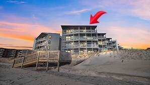 A multi-story hotel with a modern design, located on a sandy beach with a wooden staircase leading to the entrance. - Shipwatch 1411 - Point Unit (North Topsail Beach)