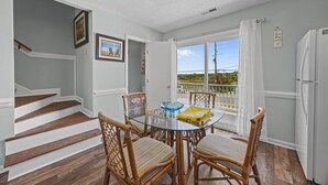 A dining area with a glass table and wicker chairs, a staircase, and a view of the outdoors. - New River Inlet Rd. 1338 (North Topsail Beach)