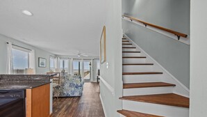 A spacious living area with a wooden staircase, a kitchen with a dishwasher, and a view to the outside. - New River Inlet Rd. 1338 (North Topsail Beach)