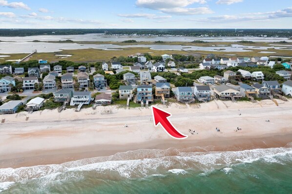 A coastal residential area with houses along the beach, a pier extending into the water, and a clear view of the ocean.