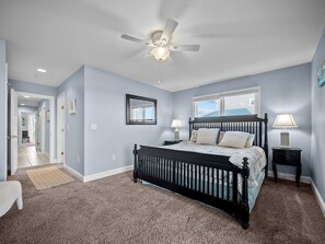 A bedroom with a bed, a ceiling fan, a window, and a nightstand.