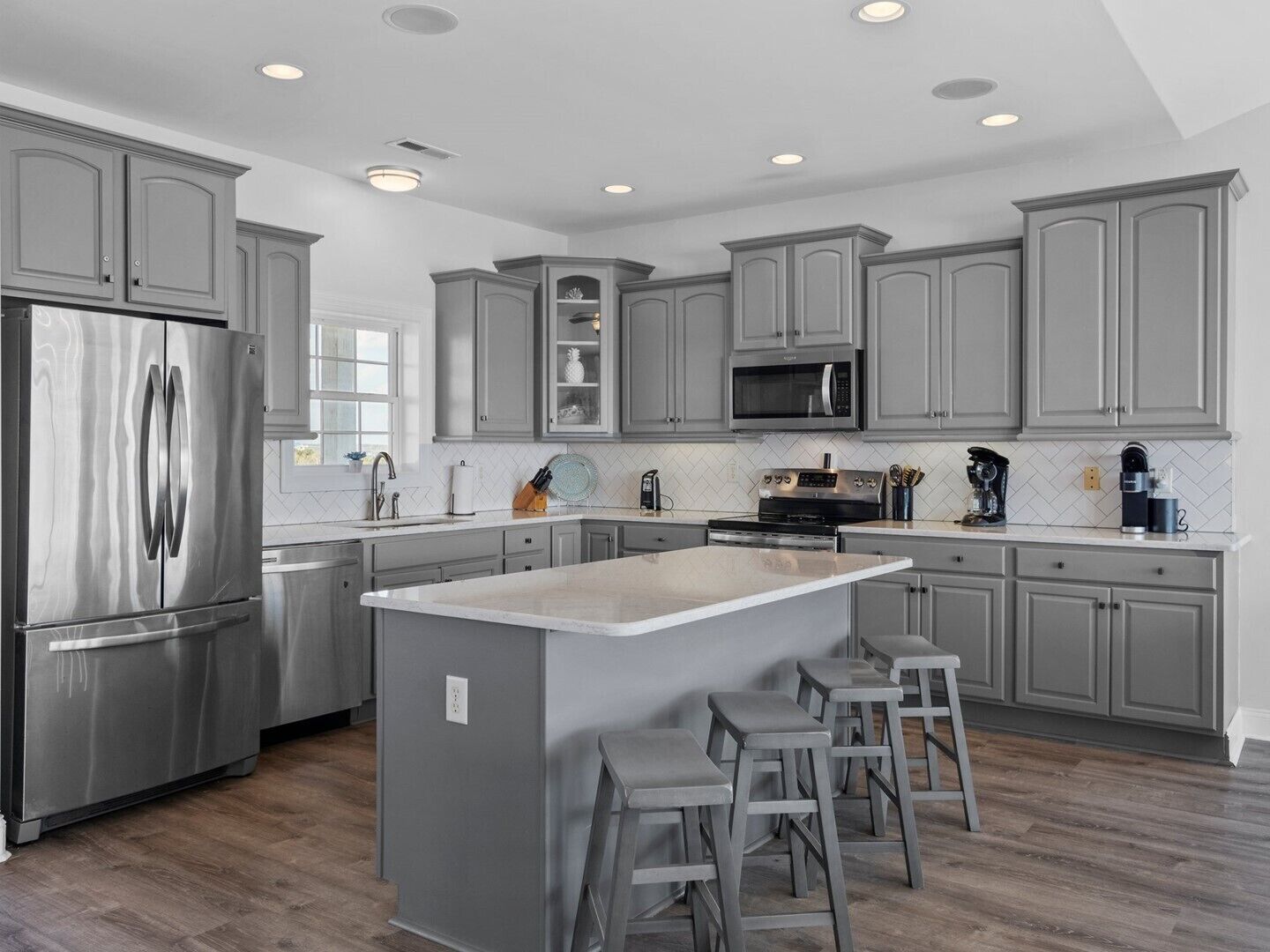 A modern kitchen with grey cabinets, stainless steel appliances, and a central island with stools.