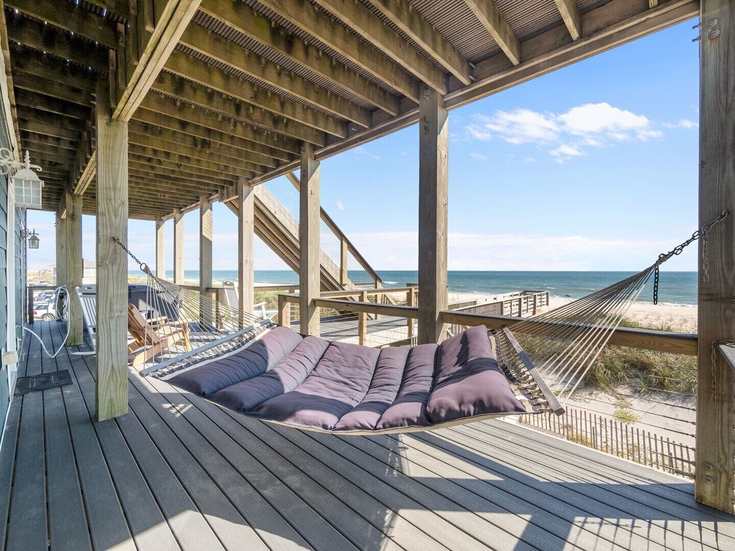 Une terrasse en bois avec un hamac et un coin salon confortable donnant sur une plage.