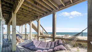 Eine Holzterrasse mit einer Hängematte und einer gepolsterten Sitzecke mit Blick auf einen Strand.