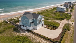 Une maison à deux étages dotée d’un balcon, située près d’une plage au rivage sablonneux et offrant une vue sur l’océan.