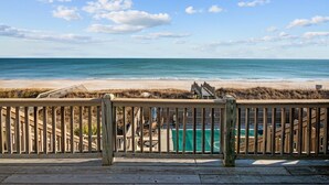 Eine Holzterrasse mit Blick auf einen Strand und eine klare Sicht auf das Meer und die Küste im Hintergrund.