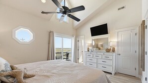 Ein Schlafzimmer mit einem Bett, einem Deckenventilator, einem Schminktisch, einem Fernseher und Blick ins Freie.