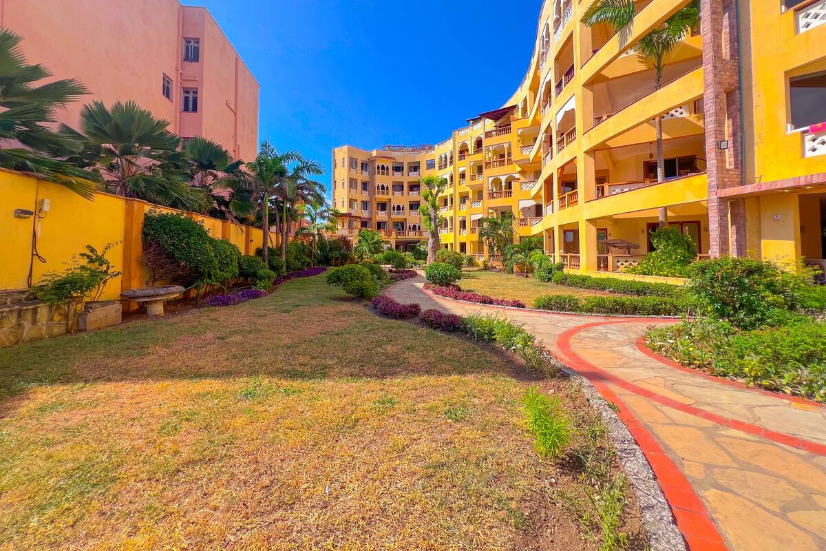 Un patio con un sendero central, rodeado de edificios amarillos de varios pisos con balcones y abundante vegetación.