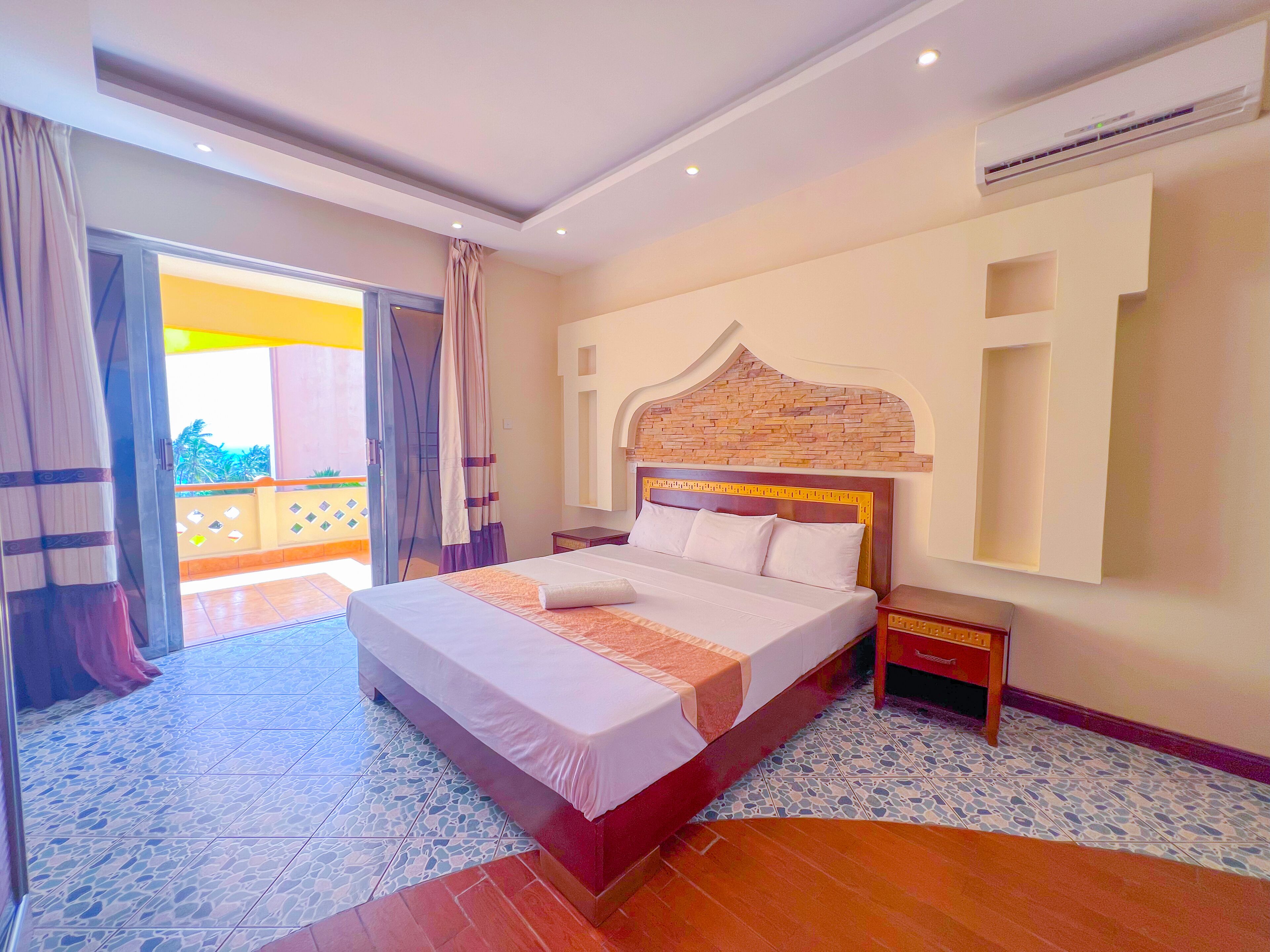 A bedroom with a bed, nightstands, a wall-mounted air conditioner, and a balcony view.