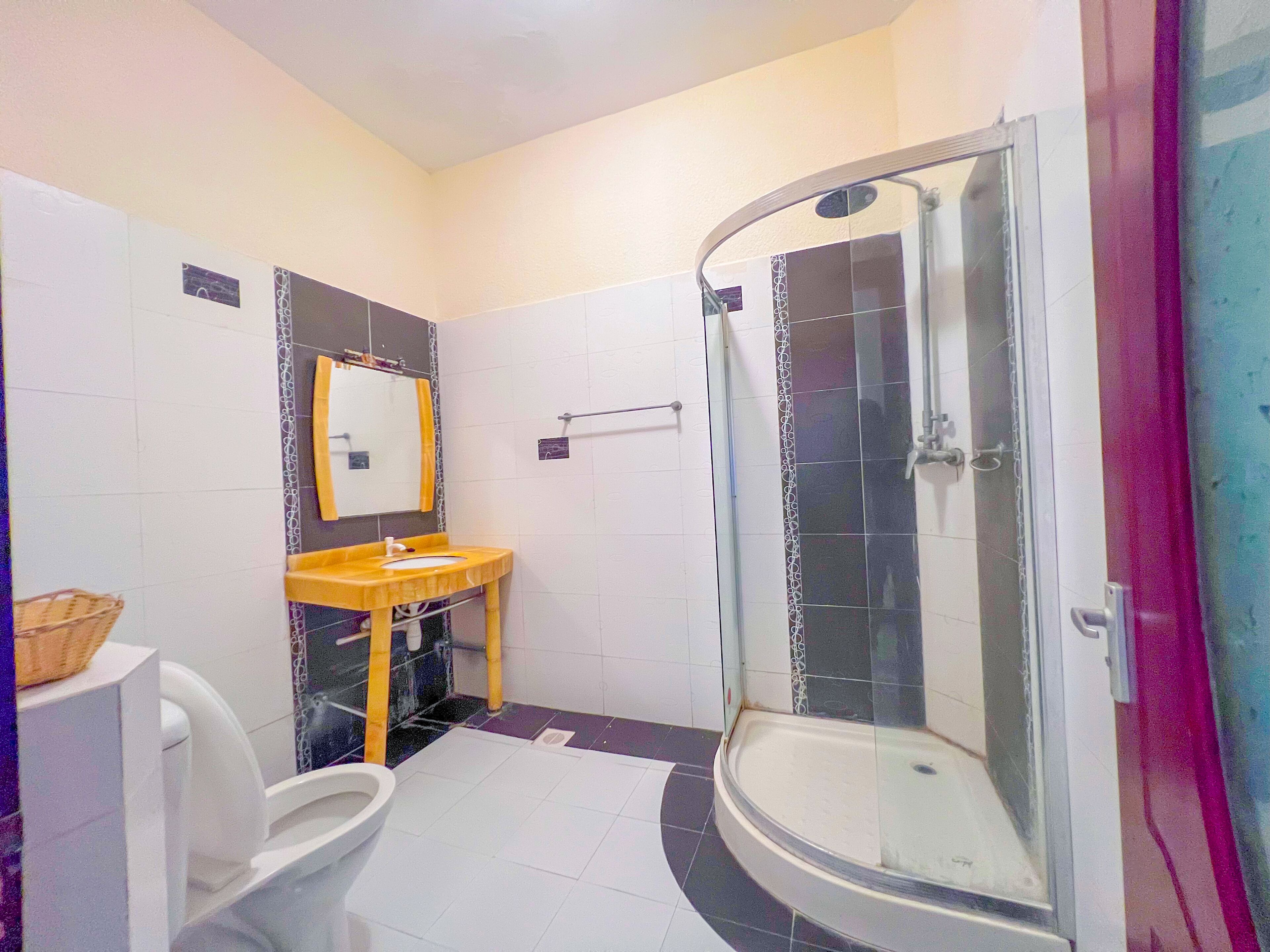 Un baño con inodoro blanco, lavamanos de madera, espejo y ducha con cerramiento de vidrio.