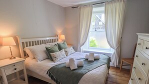 Ein ordentlich eingerichtetes Schlafzimmer mit Bett, Nachttischen, einer Kommode und einem Fenster mit Vorhängen.