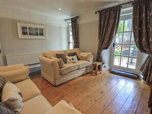A living room with a beige sofa, a small wooden table, and a window with curtains. - Brook Cottage (Windermere)