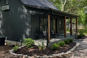 Una casa de fusta fosca amb un porxo cobert, mobiliari exterior i un petit jardí.