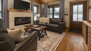 Una sala de estar acogedora con chimenea, sofás de cuero, una mesa de centro y ventanas grandes con cortinas.