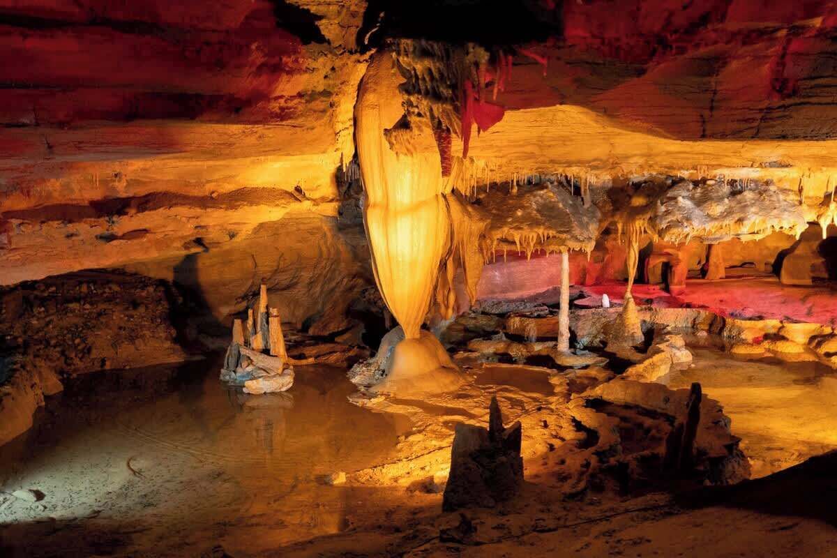 Una cueva con estalactitas y estalagmitas, iluminada con luz artificial.