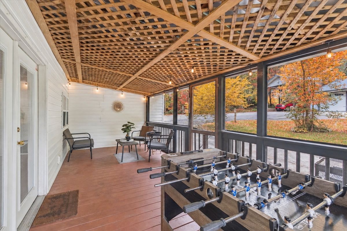 A covered outdoor area with a wooden table and chairs, a patio door, and a view of a residential street.