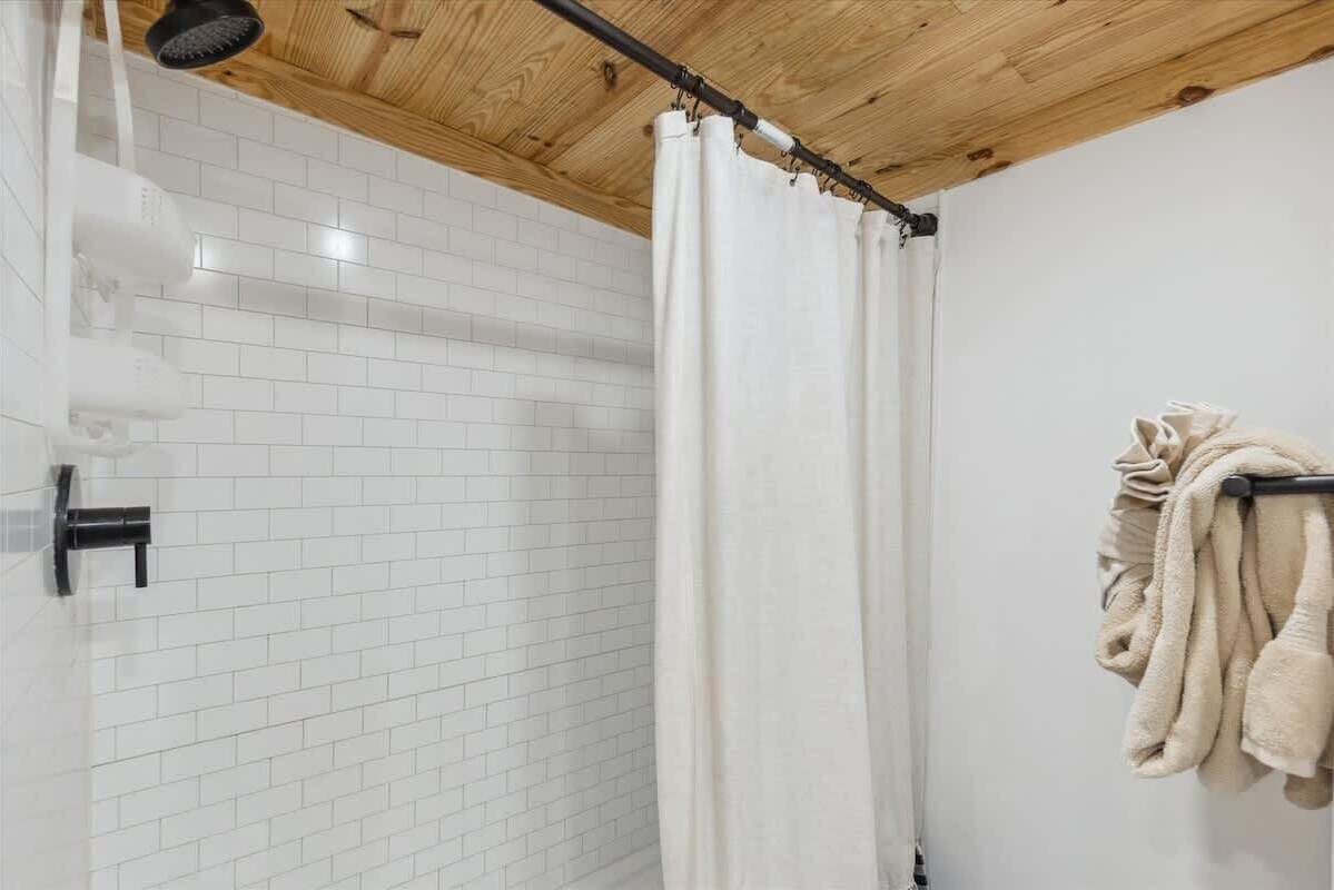 A shower with a white curtain, a towel rack with towels, and a wooden ceiling.