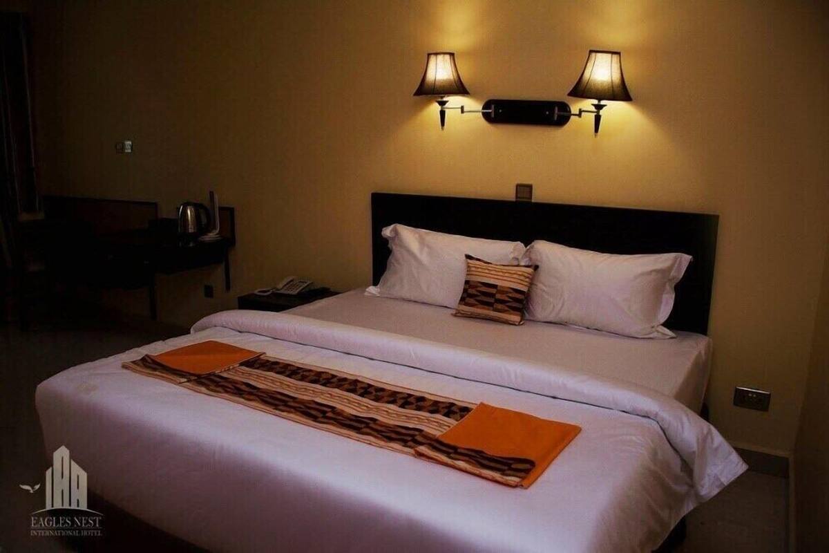A hotel room with a bed, two wall-mounted lamps, a bedside table with a phone, and a decorative throw blanket.