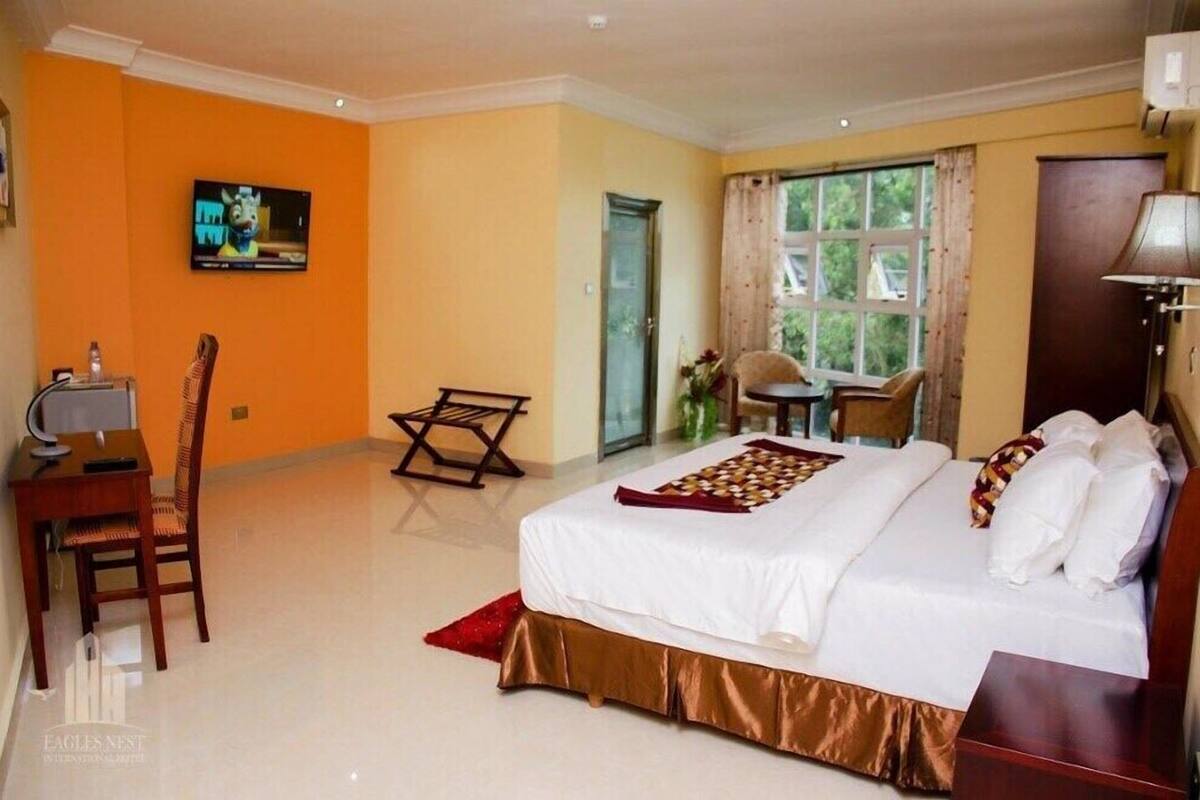 A hotel room with a bed, a desk with a chair, a television, and a window with curtains.