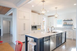 Una cocina moderna con armarios blancos, una isla central con lavavajillas, electrodomésticos de acero inoxidable e iluminación colgante.