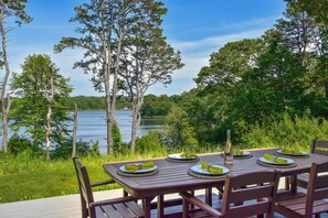 A wooden deck with a table set for four, overlooking a lake surrounded by trees.