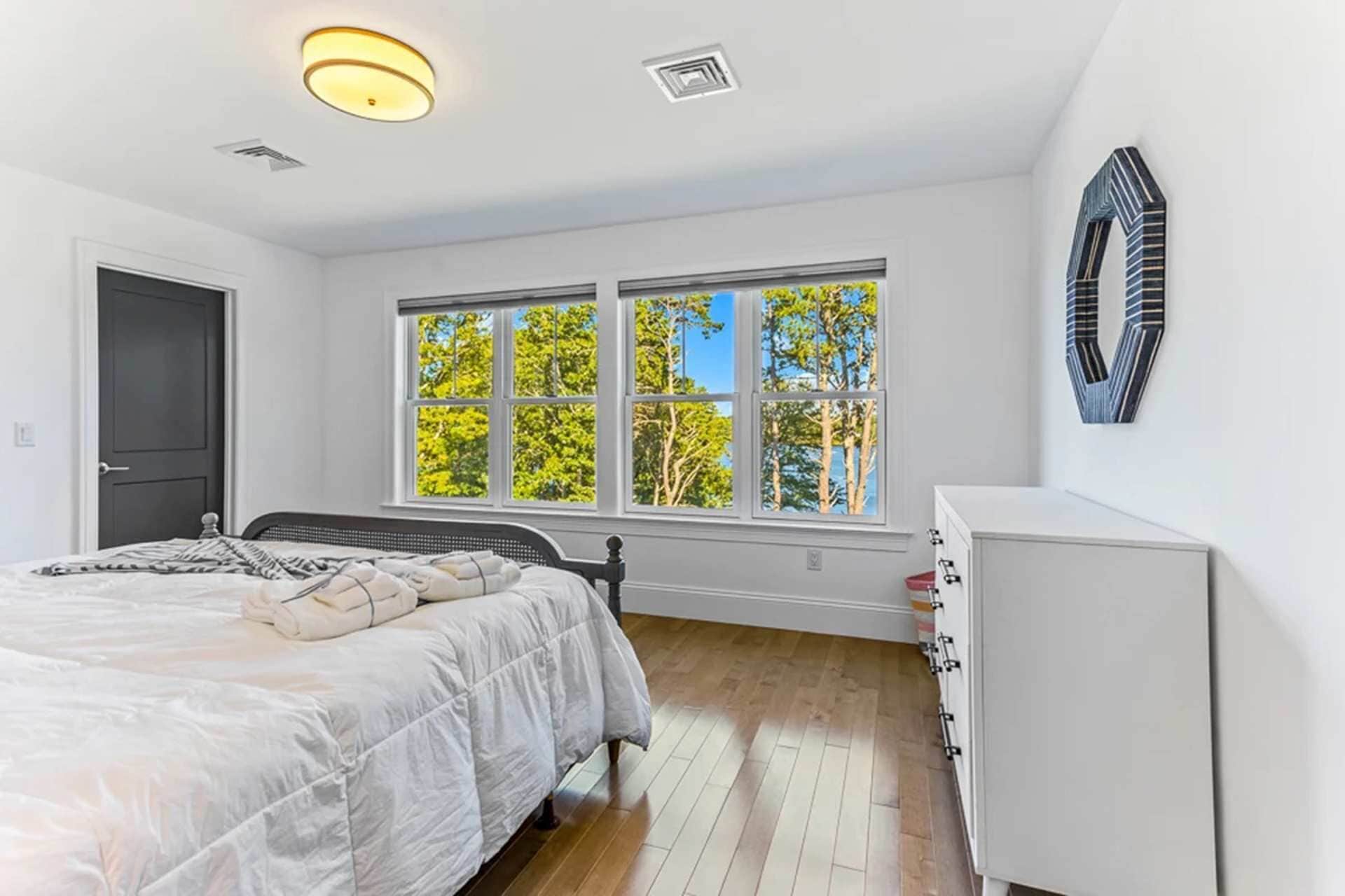A bedroom with a bed, a dresser, a window with a view of trees, and a door.