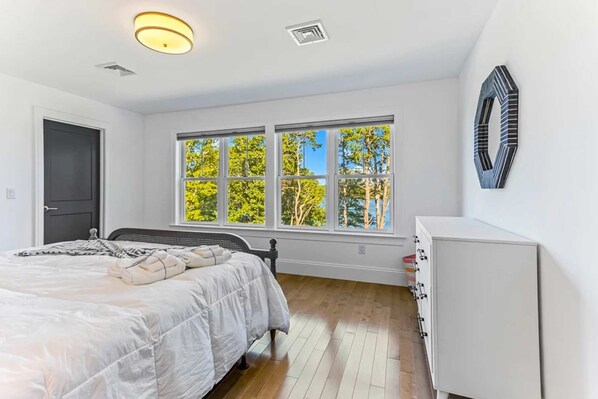 Un dormitorio con cama, cómoda, ventana con vista a árboles y puerta.