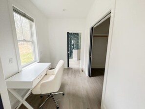 Una habitación moderna con paredes blancas, un escritorio, una silla, un ventanal y vistas a un jardín.