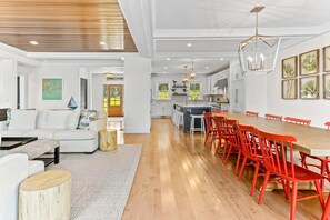 Un amplio salón con suelo de madera, un sofá blanco y una mesa de comedor con sillas rojas.