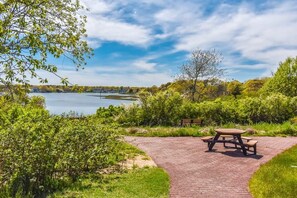 Un área de picnic con mesa y bancos, rodeada de vegetación y vistas a un lago.