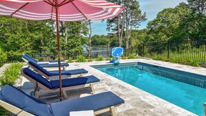 A swimming pool with lounge chairs and a basketball hoop, surrounded by trees and a fence.