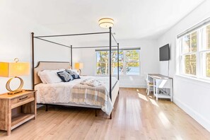Un lit à baldaquin avec des colonnes aux quatre coins, des lampes de chevet, une table de chevet en bois, un bureau avec une chaise et un téléviseur fixé au mur.