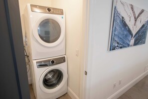 A laundry area with a front-loading washer and dryer stacked on top of each other. - Luxury Waterfront Home w/ Heated Pool and Hot Tub (Yarmouth)